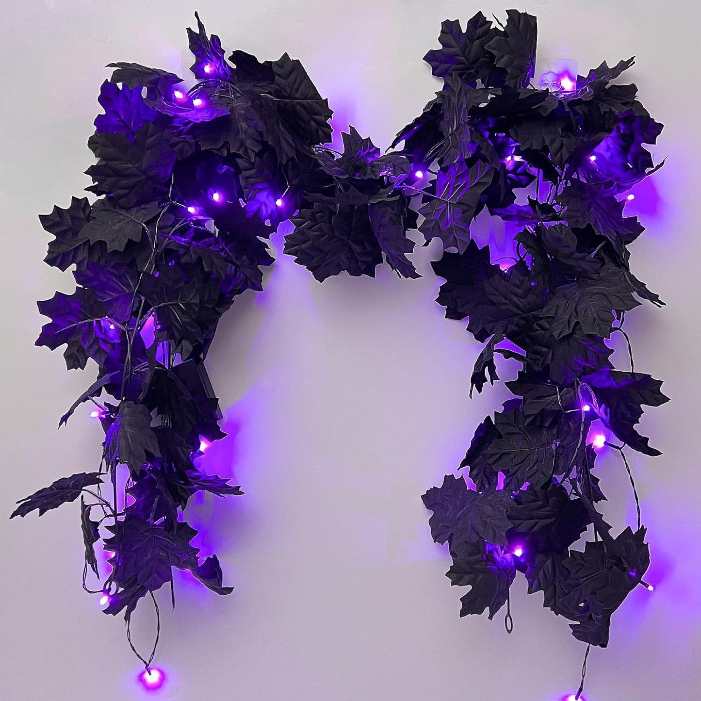 Decorative wreath with black leaves and purple LED lights on a white background