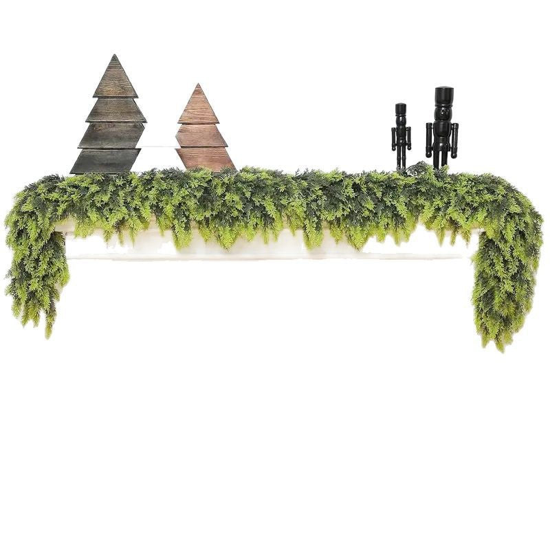 Decorative mantel with greenery, wooden trees, and candles on a white background