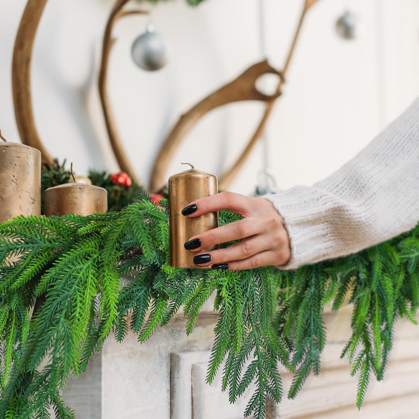 Hand holding a gold candle among greenery with a decorative wreath in the background