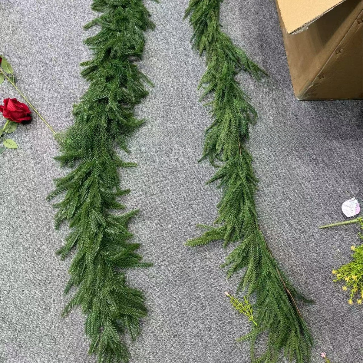 Green artificial garland on a gray surface with a cardboard box in the background.