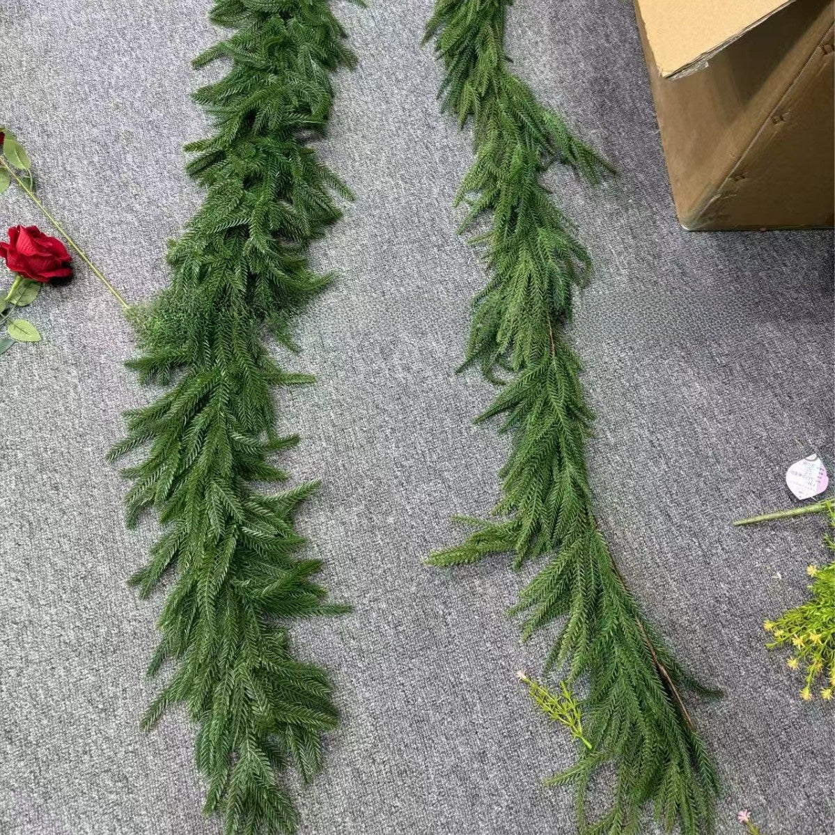 Green artificial garland on a gray surface with a cardboard box and flowers.