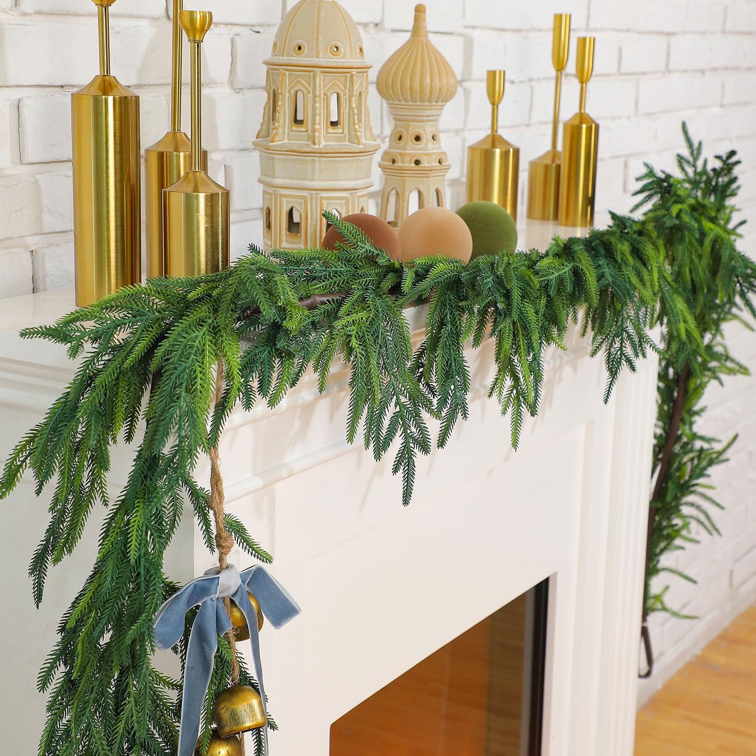 Decorative mantel with greenery, gold candles, and small buildings against a white brick wall.